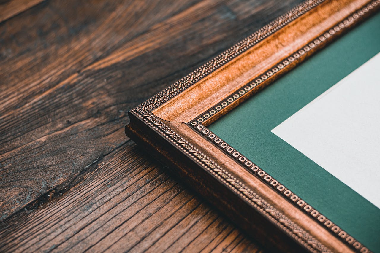 gallery-2 Close-up of a detailed antique wooden frame against a rustic wood backdrop, emphasizing vintage elegance.