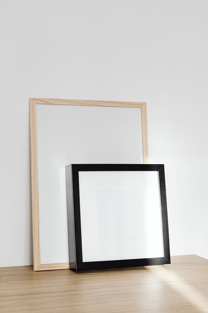 contact-img Minimalist wooden and black frames on a light wooden table in a simple, modern setting.